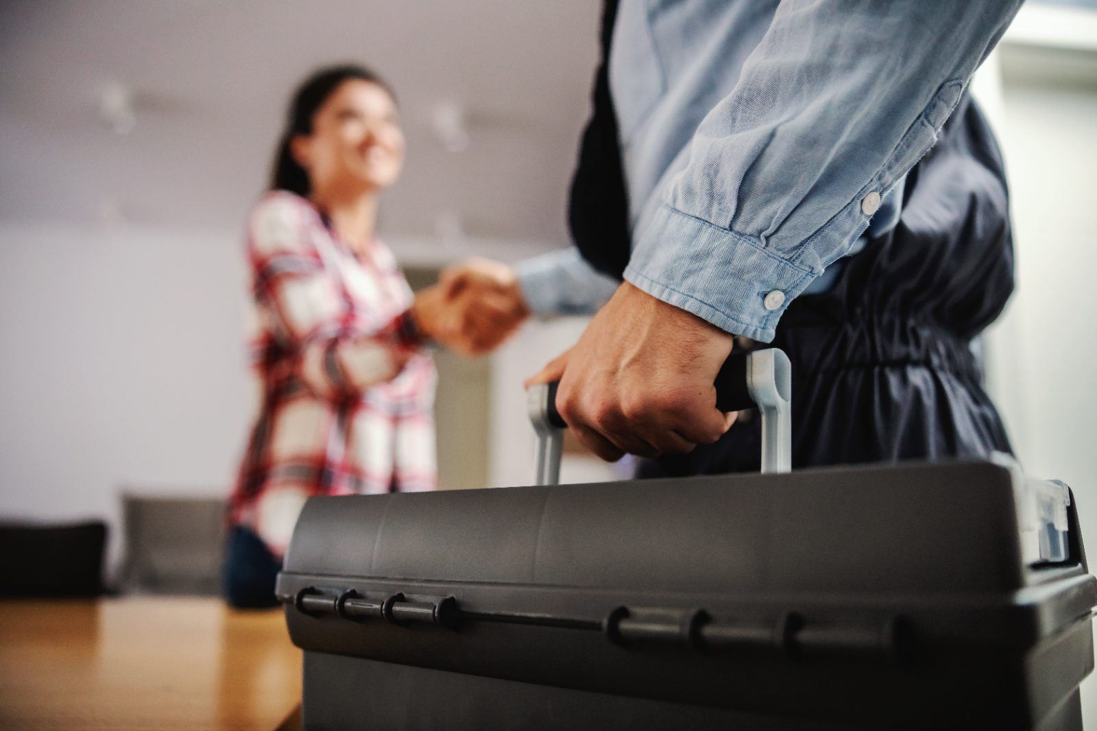 Man in denim shirt holding luggage handle with woman in plaid shirt blurred in background