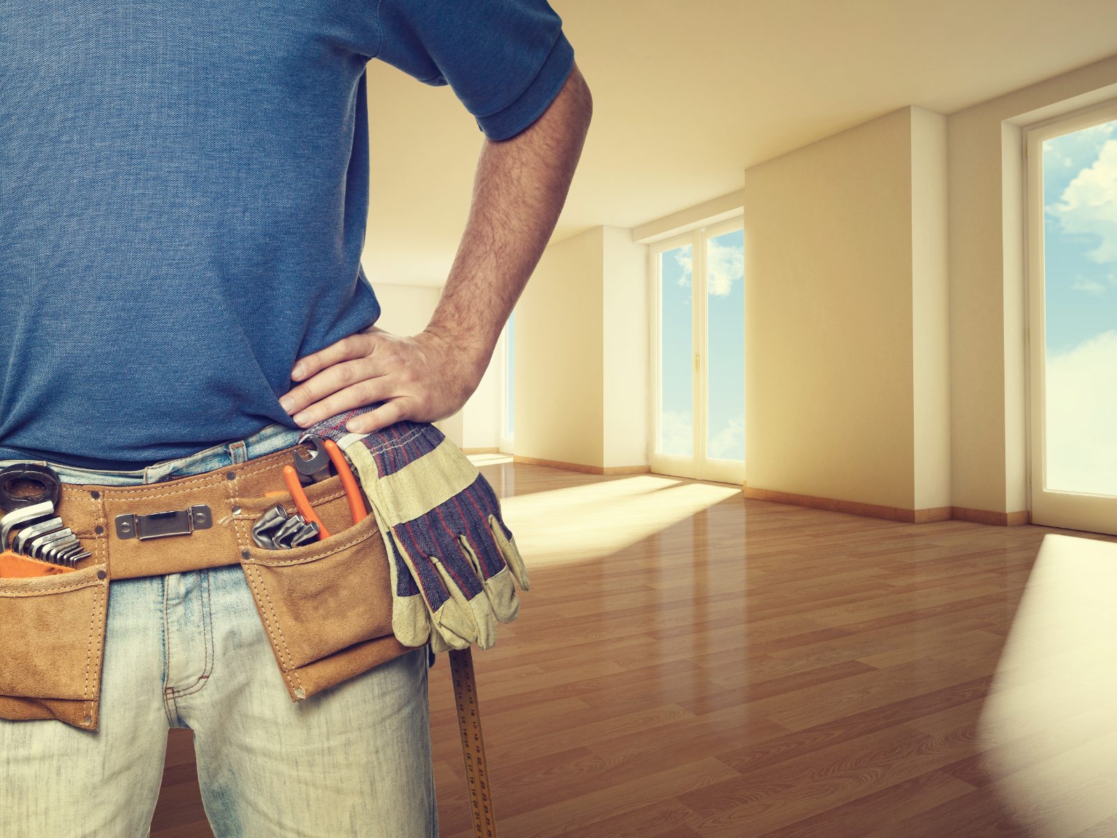 Contractor wearing tool belt standing in empty room with wooden floors