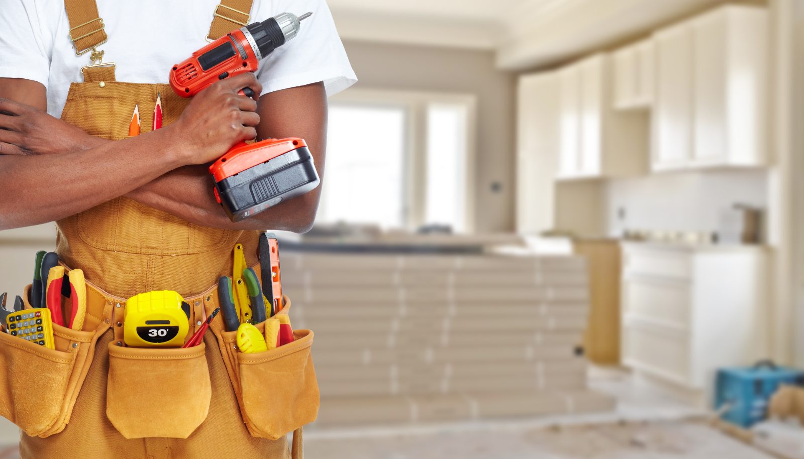 Construction worker in tool belt holding cordless drill in unfinished interior space