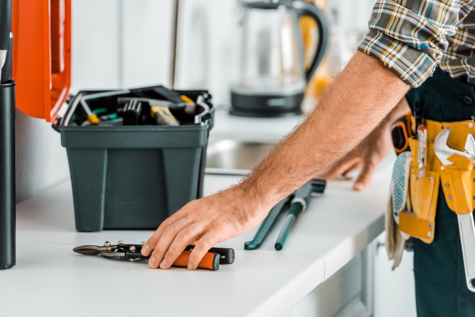 Tradesman selecting flashlight from tools on kitchen counter near toolbox and tool belt